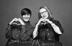 Black and white photo of Amanda Nsheiwat and Dawn Williams making a heart shapes with their hands and smiling. PC: Studio JK/The Portraits Lounge